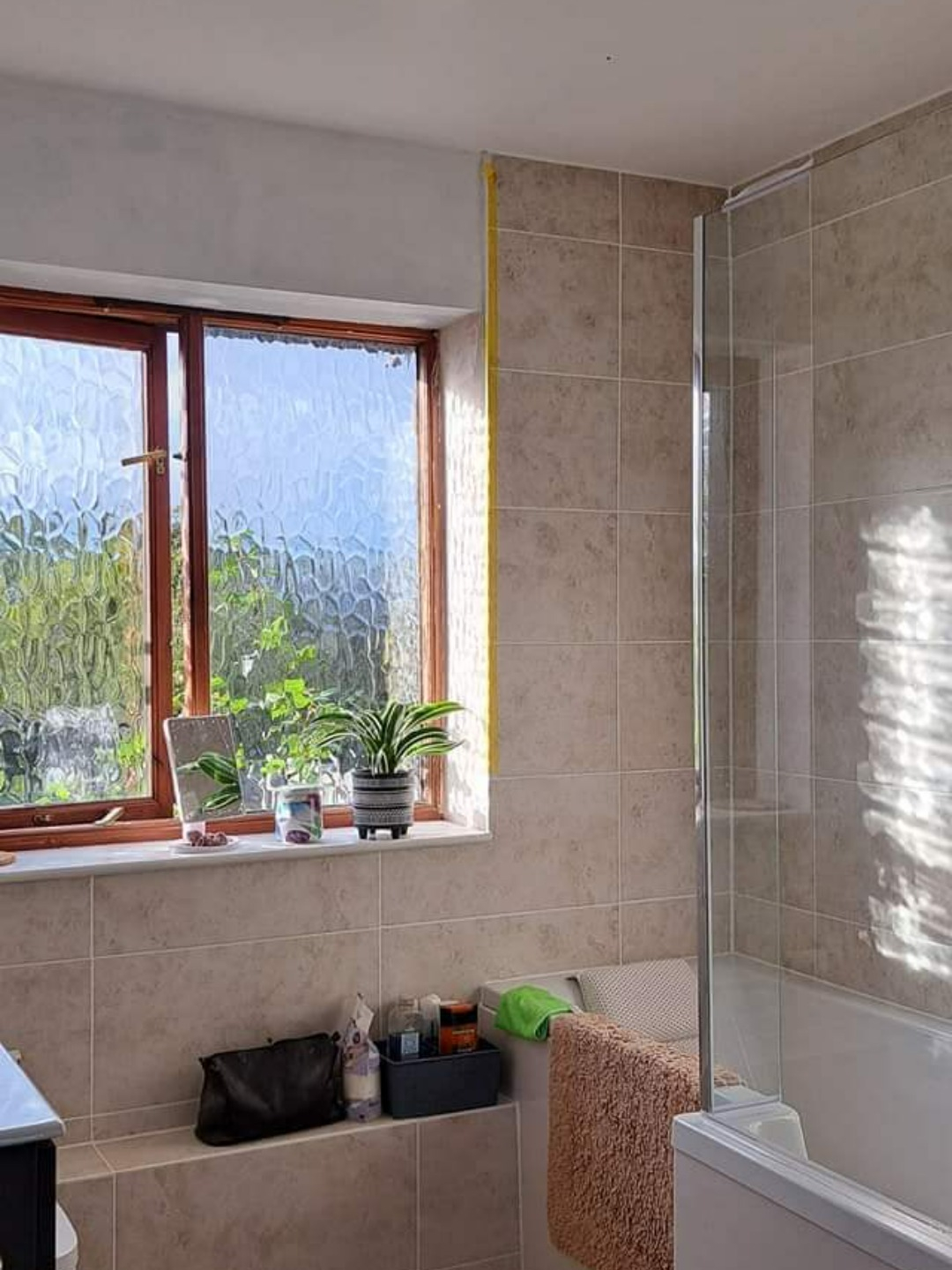 Bathroom installation with beige tiles shower over bath and shower screen